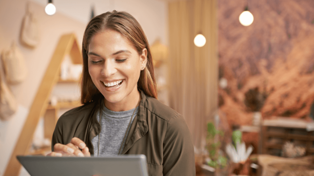 A businesswoman smiling while using a tablet in her store, emphasizing the benefits of AI tools for entrepreneurs in managing and growing their businesses.